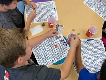 Children playing bingo with coins and markers.