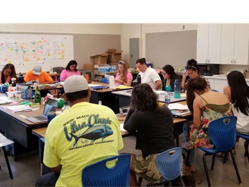 Group of people seated around tables in a classroom.