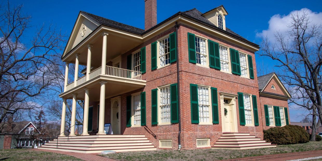 A large brick historical house with green shutters and white pillars.