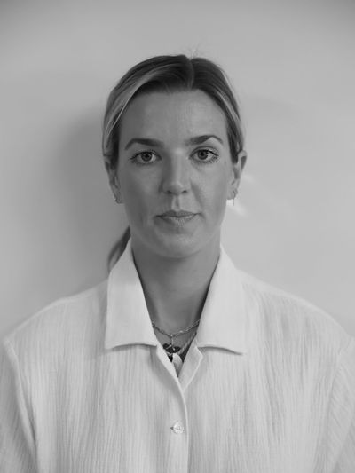 Black and white portrait of a woman in a white shirt looking directly at the camera.