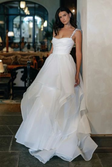 Woman in a flowing white gown leaning against a wall indoors.