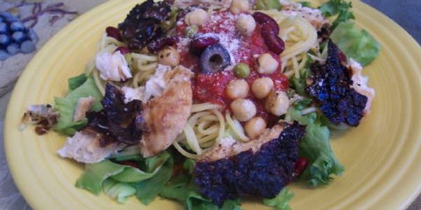 Plate of spaghetti with tomato sauce, chickpeas, olives, chicken, and leafy greens.