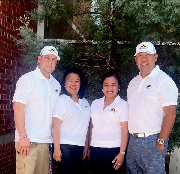 Four people wearing matching white shirts and caps, smiling outdoors.