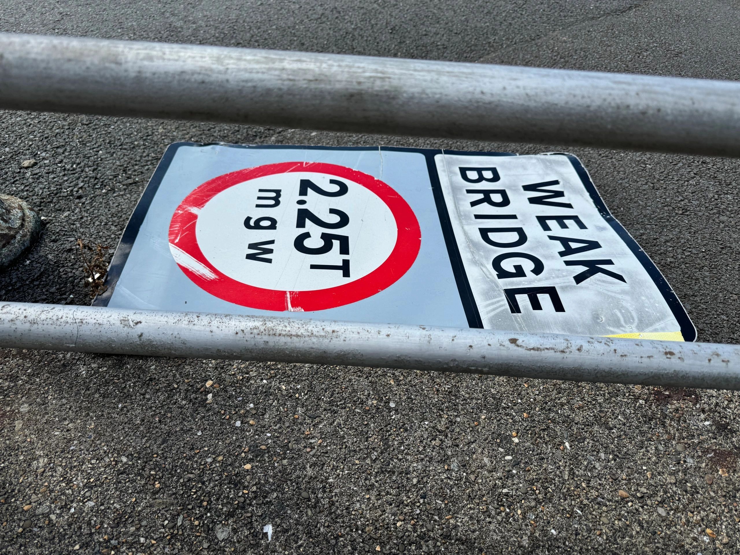 Fallen street sign on asphalt indicating weight and width limits.