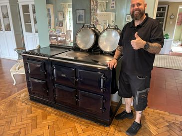 Man giving thumbs up next to a large vintage stove in a cozy room.