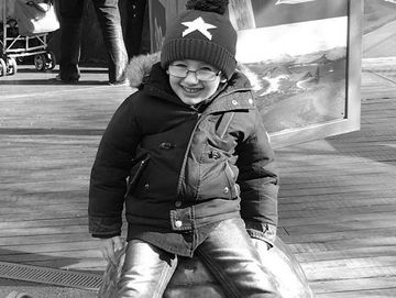 A child wearing a blue star hat sitting happily on a metal turtle sculpture.