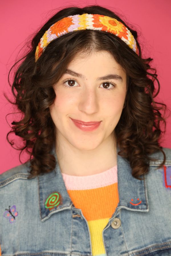 Smiling woman with curly hair and colorful headband against a pink background.