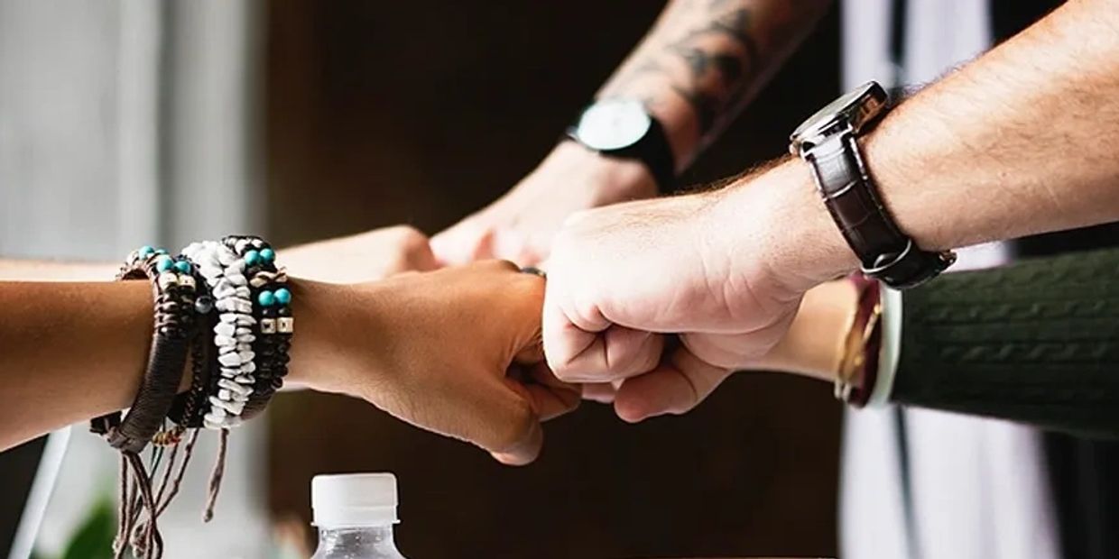 Four people doing a group fist bump showing unity and teamwork.