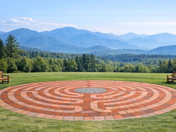 A circular brick labyrinth set on a grassy field with mountains in the background.