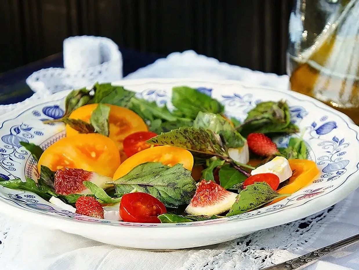 Fresh salad with heirloom tomatoes, strawberries, greens, and cheese on a decorative plate.