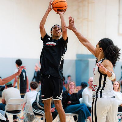 A basketball player jumps to shoot while defended by an opponent.