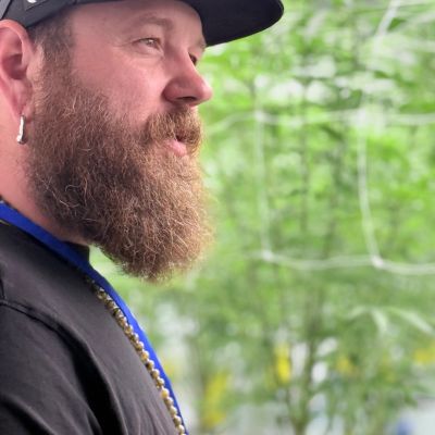 Bearded man in black cap smiling outdoors.