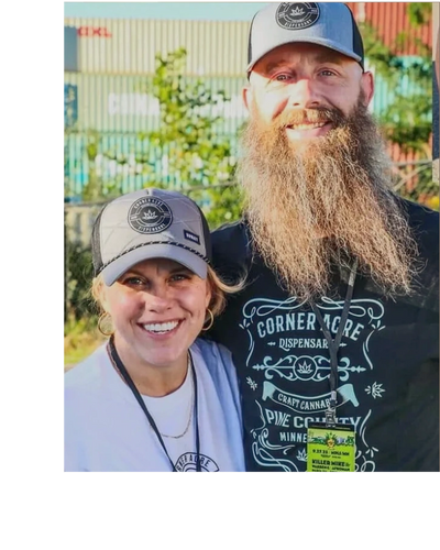 Smiling couple wearing matching hats and event badges outdoors.