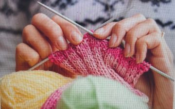 Hands knitting with pink yarn and colorful wool balls.