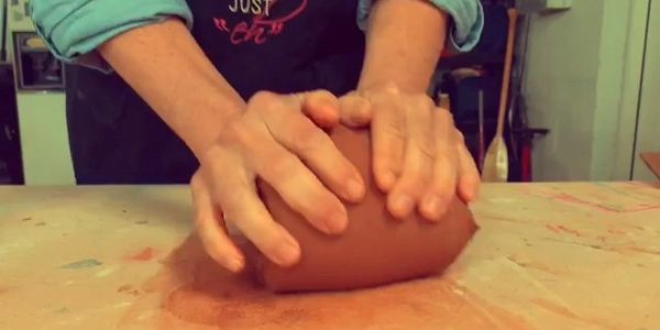 Hands kneading clay on a work surface.