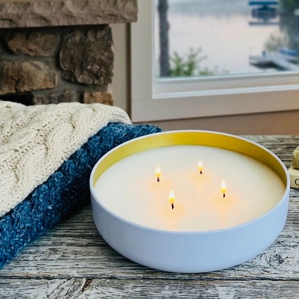 Cozy candlelit setting with books and blankets by a lakeside window.