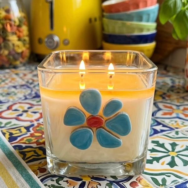 Square glass candle with blue flower design, lit with two flames.