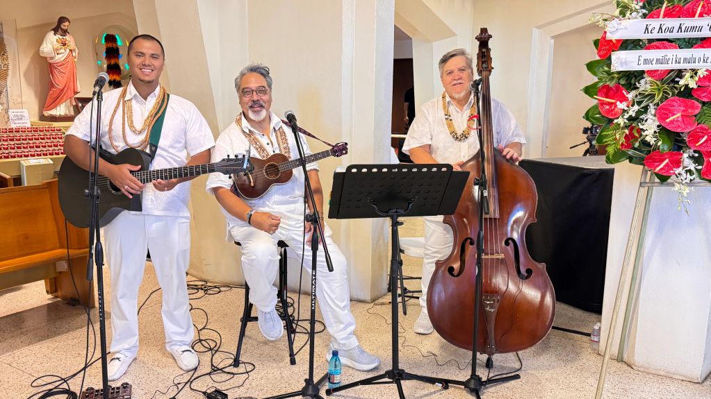 Three musicians in white playing string instruments indoors.