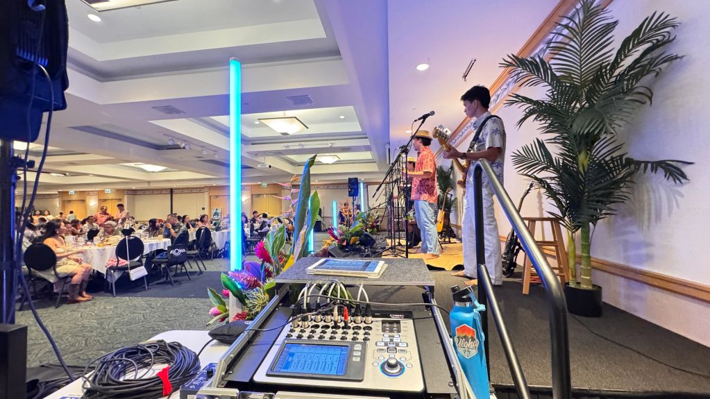 Band performing at an indoor event with seated audience.