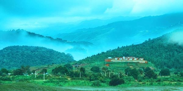 Misty hills with a house nestled among greenery and mountains in the background.