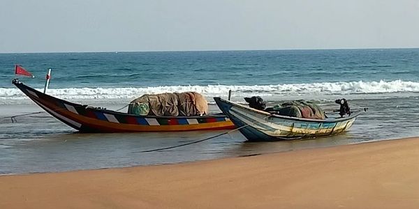 Two colorful fishing boats anchored on a sandy beach by the ocean.