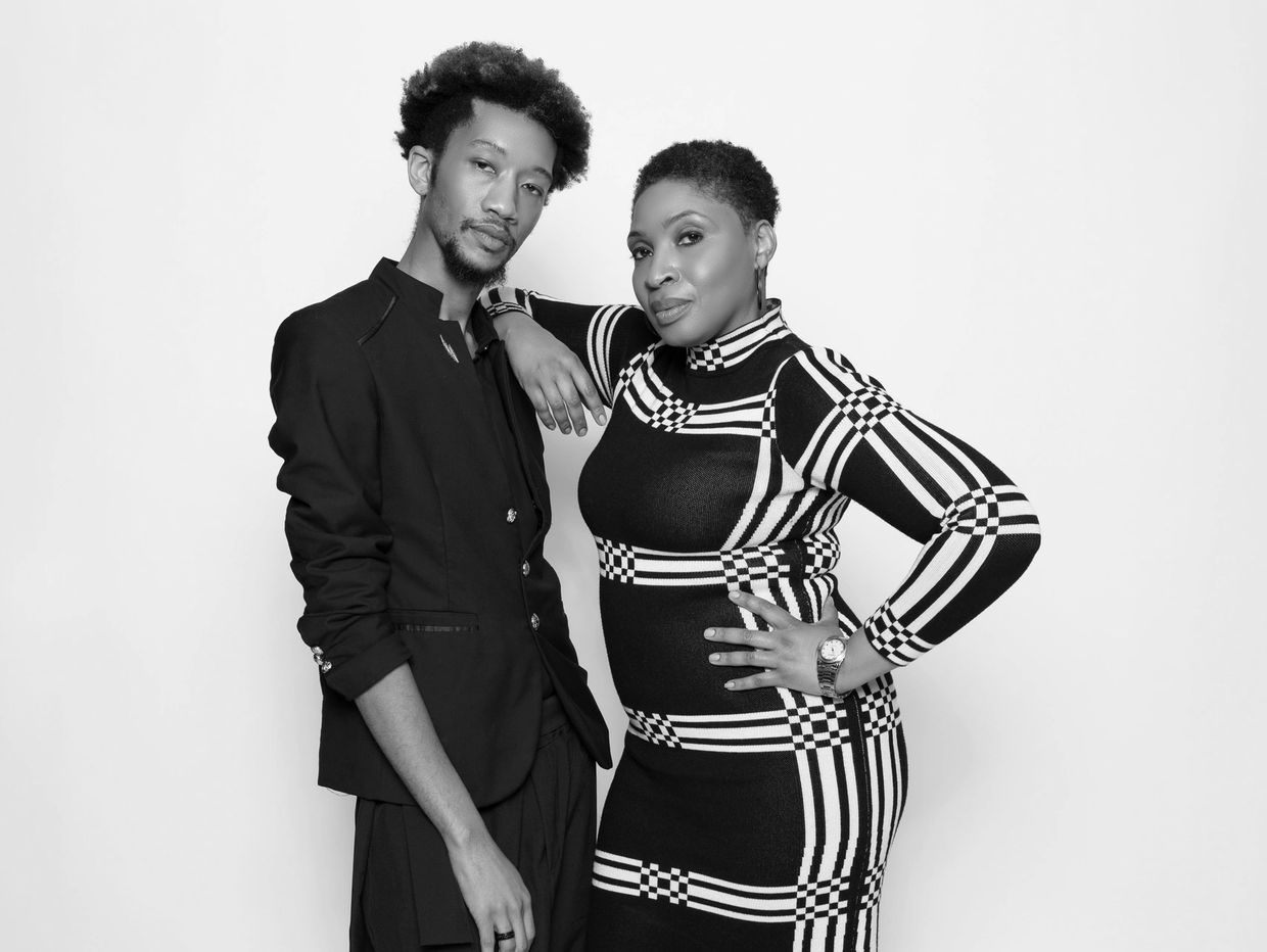 Two stylish individuals posing confidently in black and patterned outfits against a white backdrop.