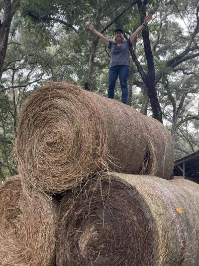 Person standing on a large hay bale with arms raised.