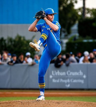 Baseball pitcher in blue uniform winding up for a pitch on the mound.