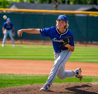 Baseball pitcher in blue uniform throwing a pitch on the mound.
