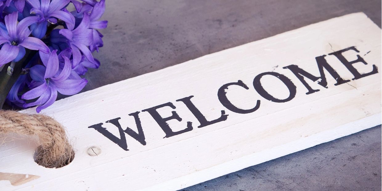 A rustic welcome sign with purple flowers on a gray surface.
