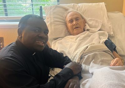 A man in black comforting an elderly person in bed.