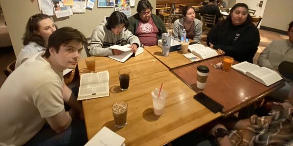 A group of people sitting around a table with open books and drinks.