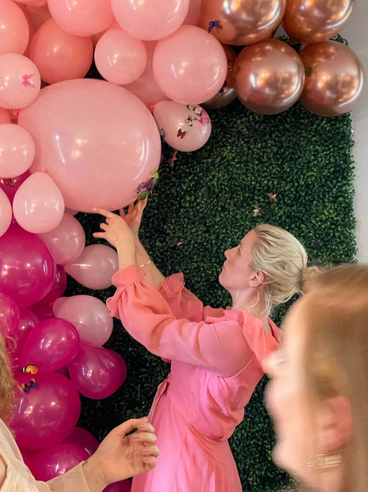 Woman in peach dress works on pink balloons.