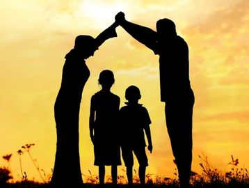 Silhouetted family forming a roof with hands at sunset.