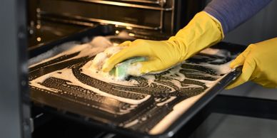 Oven cleaning: hands in yellow gloves scrubbing an oven door, removing grease for a spotless finish.