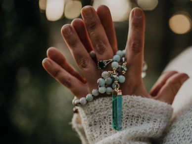 Hands holding a beaded necklace with a green pendant.
