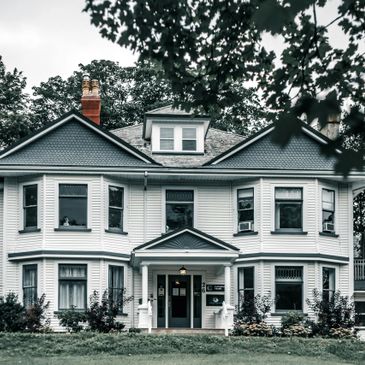 Large white two-story house with a porch and multiple windows.