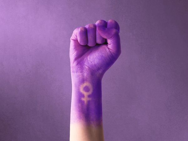 Raised fist painted purple with a female gender symbol on the wrist.