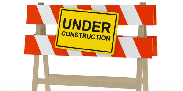 A wooden barricade with red and white stripes and an under construction sign.