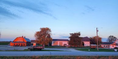 A peaceful rural farm scene at sunset with barns and trees.