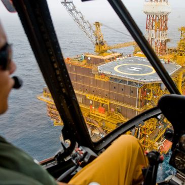 View from a helicopter cockpit approaching an offshore oil platform with a helipad.