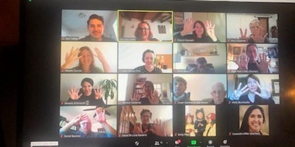 A Zoom call with 16 participants waving at the camera.