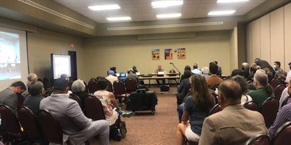 People attending a meeting in a conference room with a panel at the front.