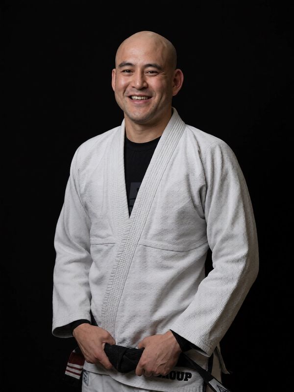 Man in a white martial arts gi holding a black belt.