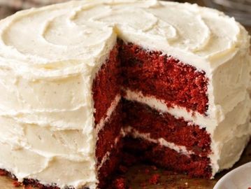 A red velvet cake with white frosting and a slice removed.