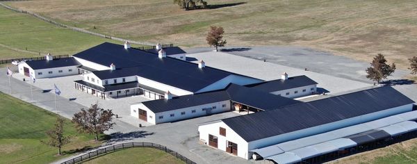 A large modern barn complex with black roofs and white walls in a rural area.