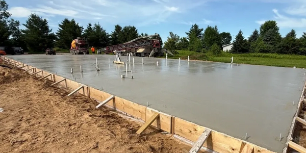 Freshly poured concrete slab foundation at a construction site under a blue sky.