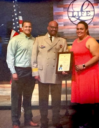 Three people posing, one in uniform holding a framed certificate.