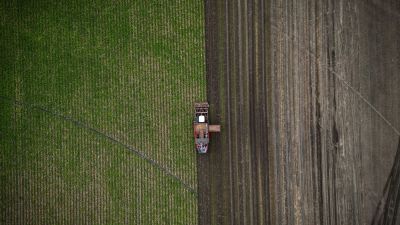 Tractor plowing a field between green and bare soil.
