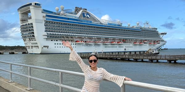 Woman posing happily in front of a large cruise ship.